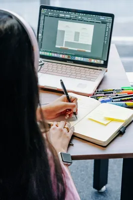 A person writing in a notebook beside an open laptop
